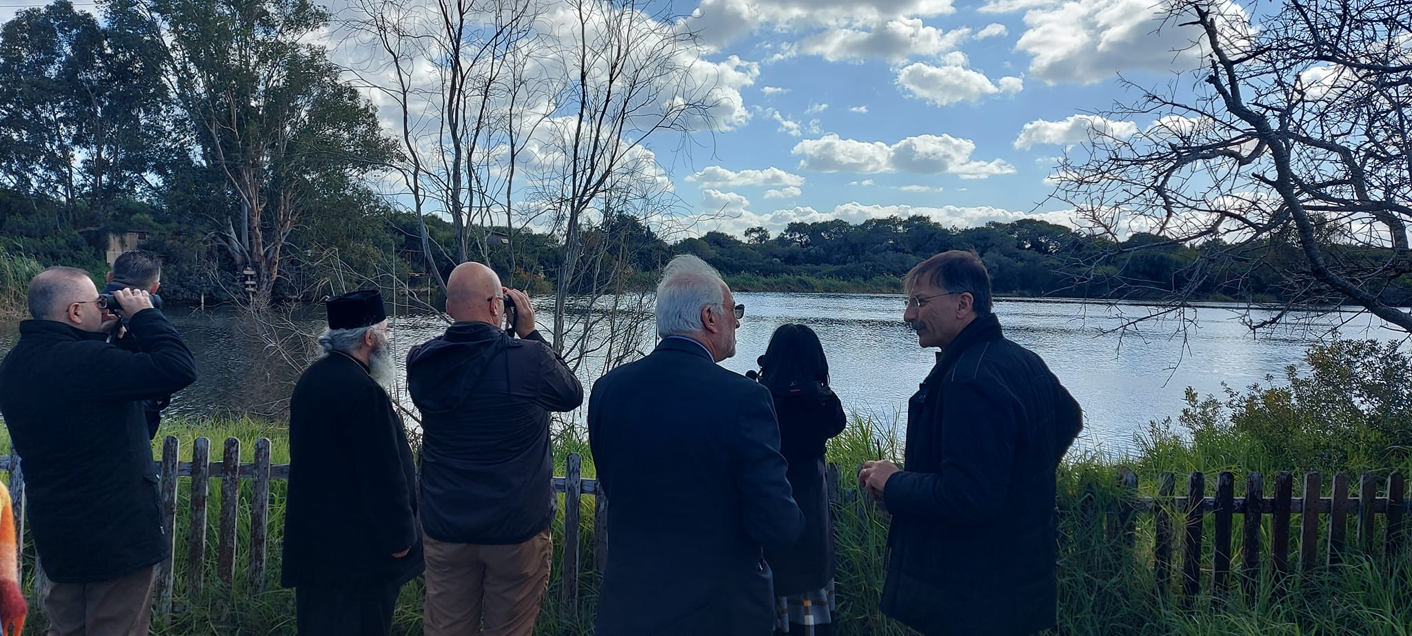 A group of people birdwatching while looking out over a lake. Some of them are discussing what they can see